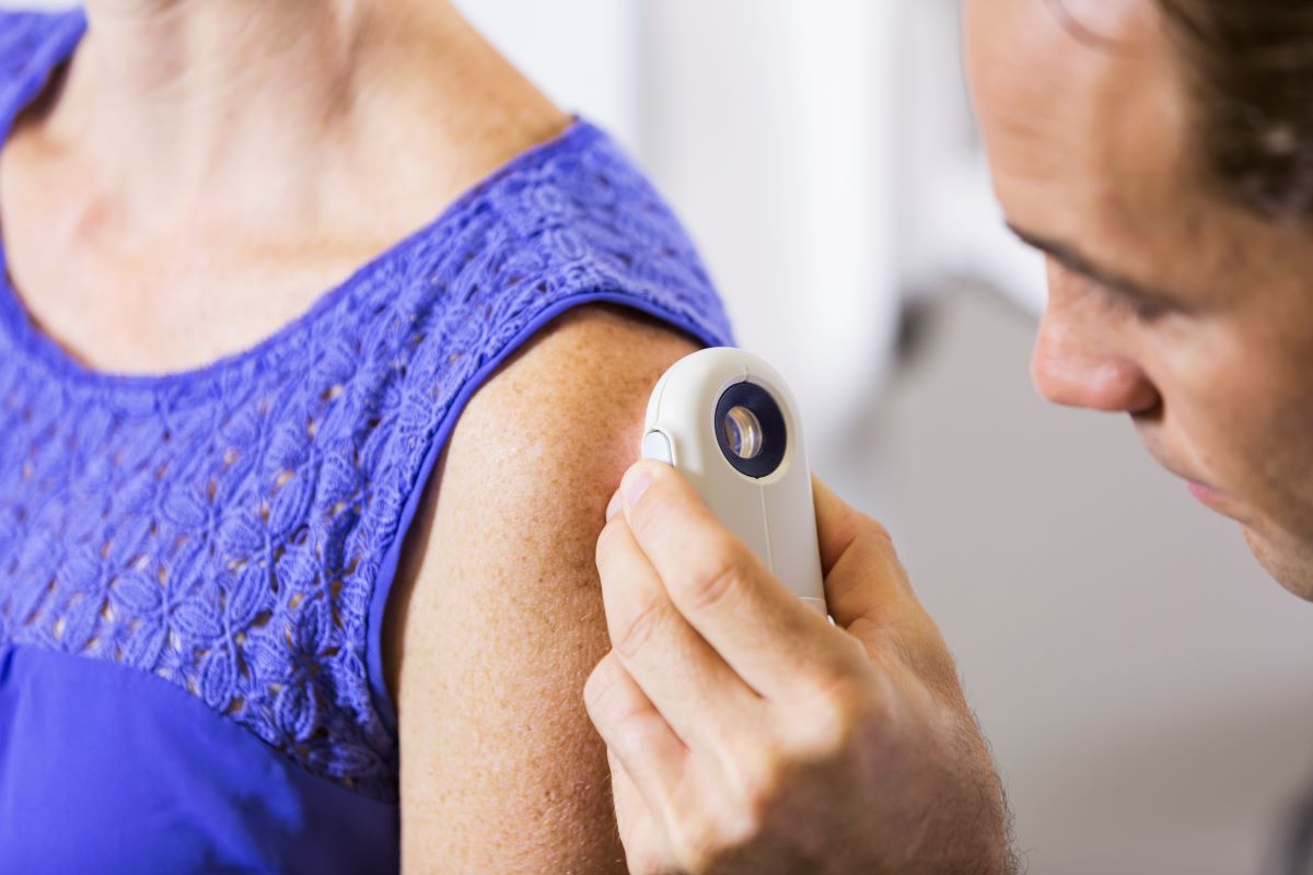 Doctor in a clinical setting using an image enhancing device to look directly at a female patients arm