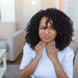 Woman touching her sore throat and grimacing.