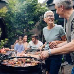 Man and woman standing at a grill at a small barbecue.