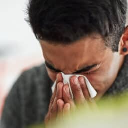 Man holding tissue to nose sneezing