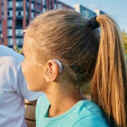 Child with hearing aid listens to her parents.