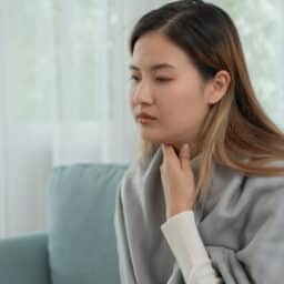 Woman with allergies holds her sore throat and looks sad.
