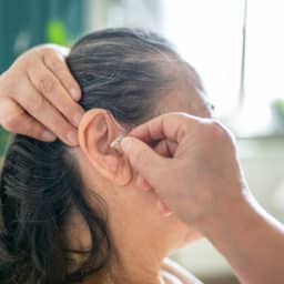 Woman takes her hearing aid out in order to clean it before bed.