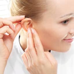 Woman inserts her hearing aid after cleaning it.