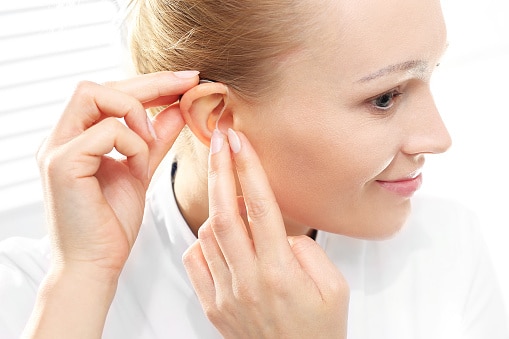 Woman inserts her hearing aid after cleaning it.