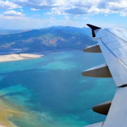 Arial view showing an airplanes wing with a massive view of a blue salt lake with a mountain range behind it in the distance